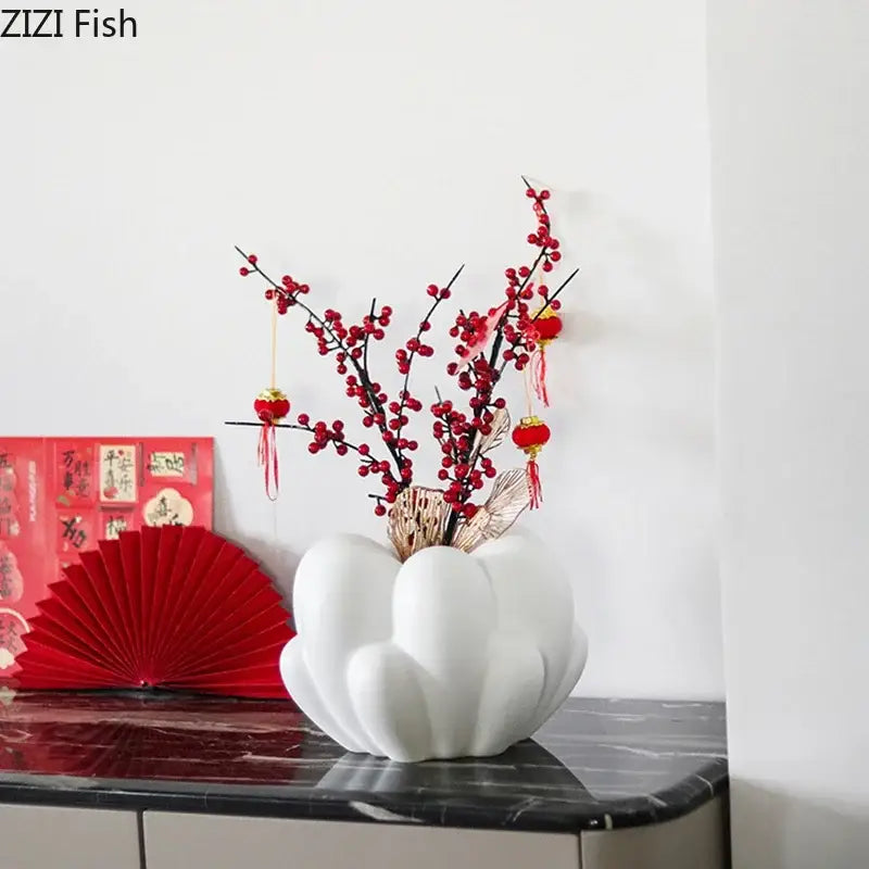 White ceramic creative petal vase with scalloped design holding red berry branches and hanging lanterns for decor