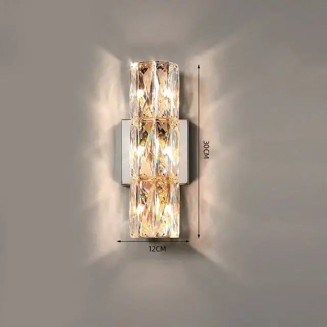 A modern decorbites crystal wall lamp with three stacked rectangular panels refracting warm golden light