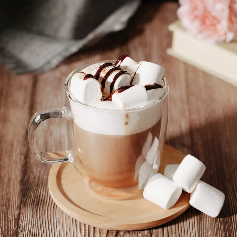 A clear double wall glass coffee cup filled with warm chocolate latte topped with whipped cream and marshmallows