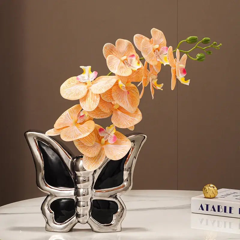 Modern silver and black butterfly ceramic vase with a glossy interior holding delicate peach orchids for living room decor