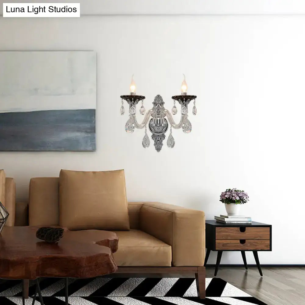 Modern silver candle wall mounted sconce with ornate crystal droplets and two lit candle-style bulbs for bedroom lighting