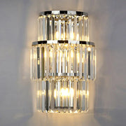Modern silver crystal three-tiered wall mounted light with cascading clear prisms and polished chrome rings emitting warm glow