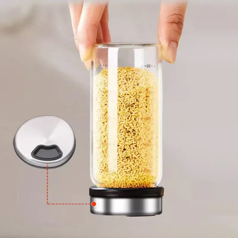 Clear glass seasoning jar with stainless steel lid and base filled with yellow granules from a modern silver set