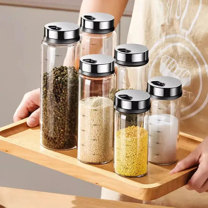 Clear glass seasoning jar set with silver metal lids and measurement markings filled with various seasonings