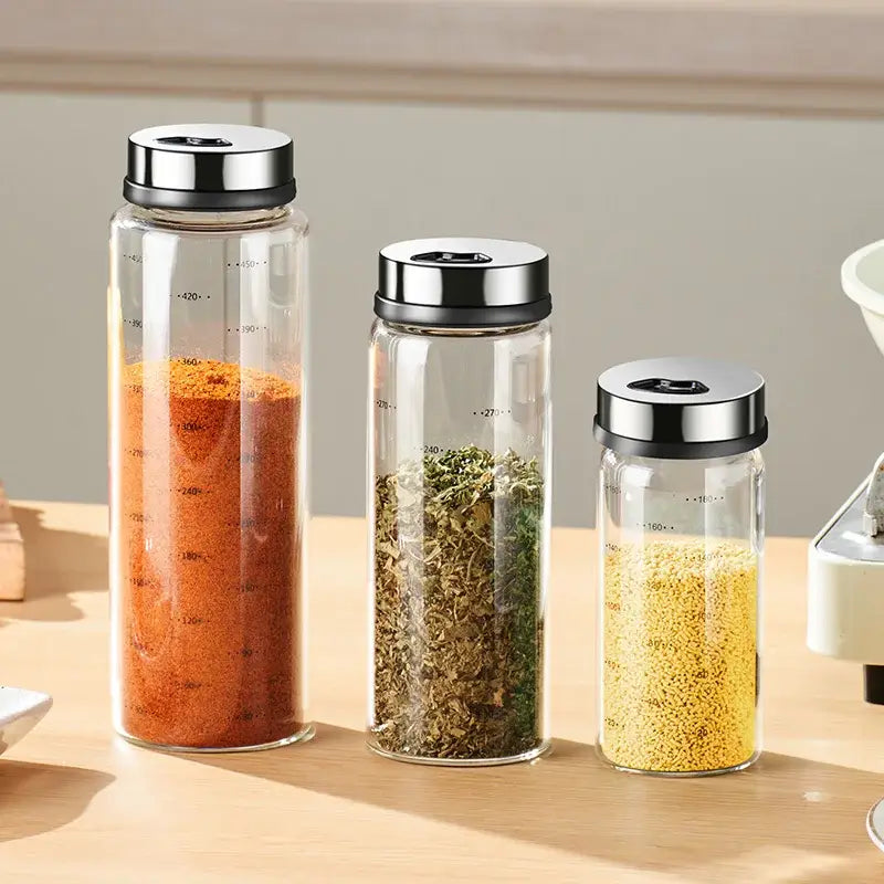 Three clear glass seasoning jars with silver lids and measurement lines in a modern glass seasoning jar set