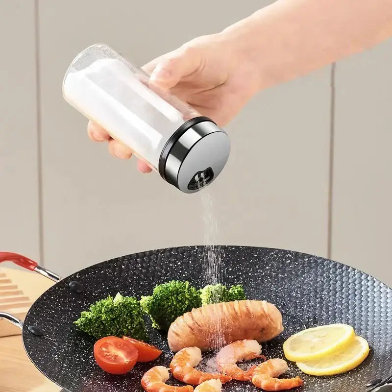 Clear glass seasoning jar with sleek silver metal cap used to season food in modern glass seasoning jar set