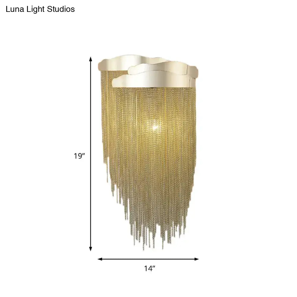 A 19-inch tall gold-toned wall lamp with tassel design metal chains and an ornate scalloped bulb base for bedroom use