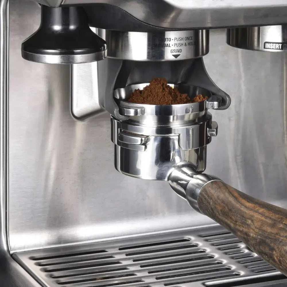 Modern silver machined stainless steel dosing funnel ring with wooden handle espresso portafilter filled with ground coffee