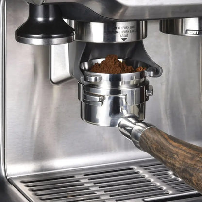 Modern silver machined stainless steel dosing funnel ring with wooden handle espresso portafilter filled with ground coffee