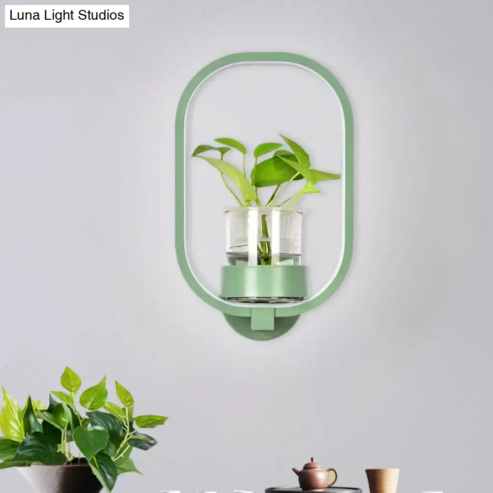 A sleek mint green oval wall light with plant pot and clear glass vase holding green leaves for 110v-120v use