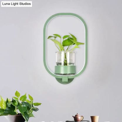 A sleek mint green oval wall light with plant pot and clear glass vase holding green leaves for 110v-120v use