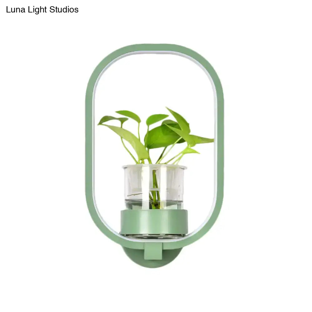 A sleek mint-green oval wall light with a silver plant pot and clear glass cup holding vibrant green leaves 110v-120v