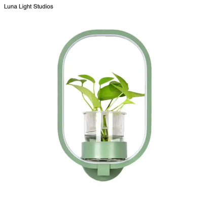 A sleek mint-green oval wall light with a silver plant pot and clear glass cup holding vibrant green leaves 110v-120v
