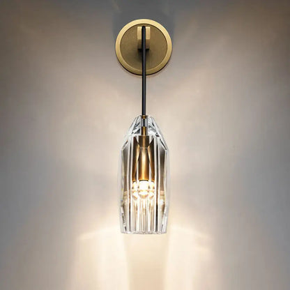 Modern single light brass wall sconce with clear crystal faceted shade and brass accents for bedroom lighting