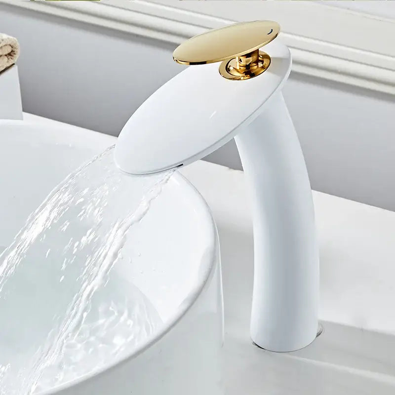 White ceramic waterfall basin faucet with gold-toned oval handle and sleek curved spout for modern bathroom decor