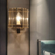 Gold-toned wall light with smoke gray glass panels and geometric cage frame for modern bedroom sconce lighting