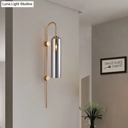 A modern smoke gray glass wall light with polished brass frame and cylindrical chrome shade for living room use