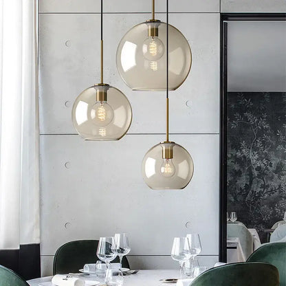 Three spherical modern smoked glass pendant lights with brass accents hanging from the ceiling for dining room use