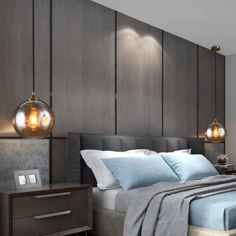 Warm amber decorbites glass ball pendant lights with gold-toned metal fixtures above a modern bed