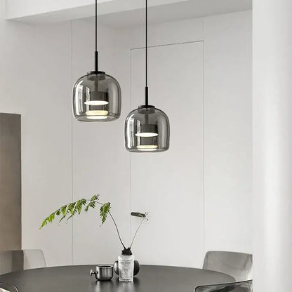 Two sleek modern smoked glass bowl chandelier pendant lights with black cords hang above a dining table