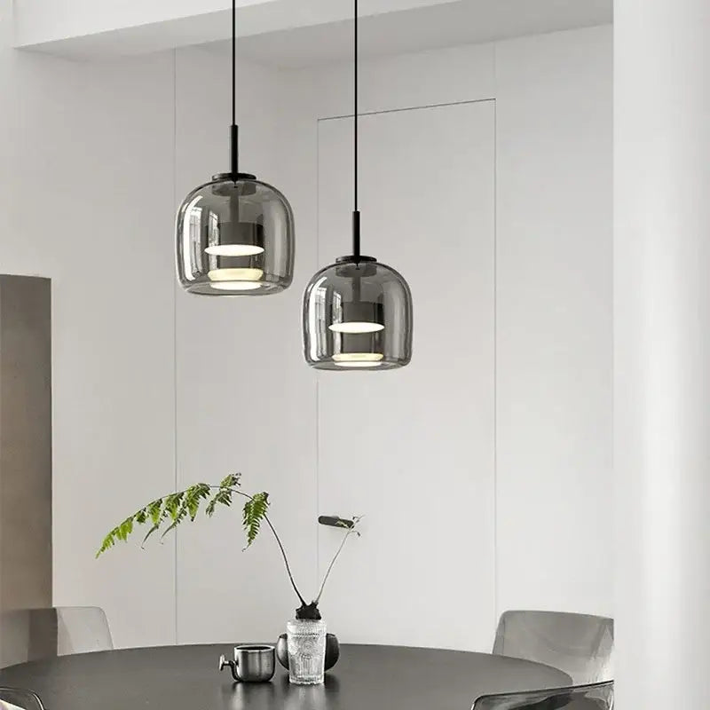 Two sleek modern smoked glass bowl chandelier pendant lights with black cords hang above a dining table