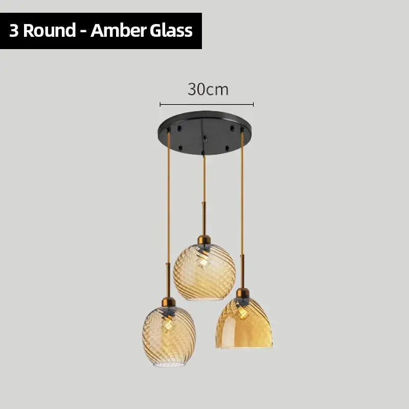 Three amber glass chandelier pendant lights with textured swirling design and brass accents for modern kitchen use