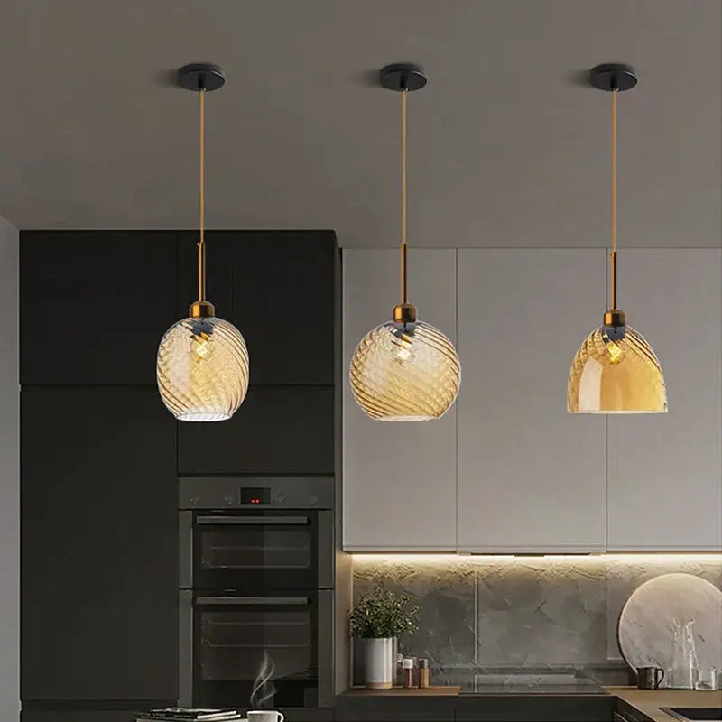 Three amber glass chandelier pendant lights with gold metal fixtures and swirling patterns for modern kitchen use