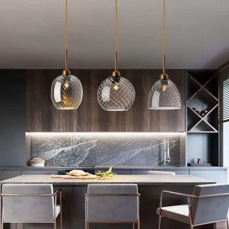 Three elegant smoked glass chandelier pendant lights with gold fixtures hang above a modern kitchen island