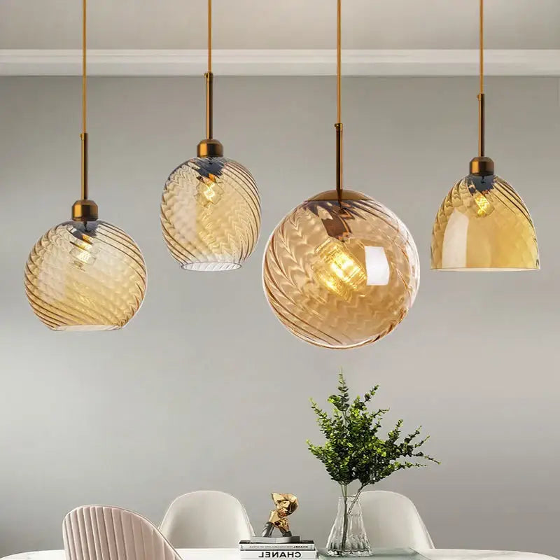Four elegant amber glass chandelier pendant lights with swirling patterns and brass-finished hardware for kitchen use