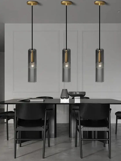Three modern pendant lights with smoked glass shades and gold-toned decorbites crystal copper fixtures above a black table