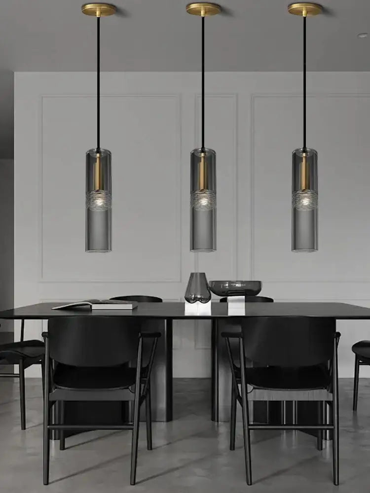 Three modern pendant lights with smoked glass shades and gold-toned decorbites crystal copper fixtures above a black table
