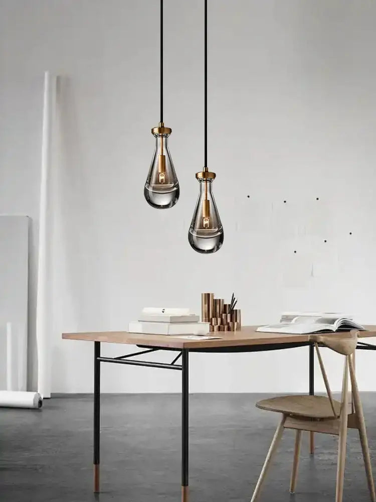 Two modern smoked glass crystal copper pendant lights with brass accents hang above a wooden desk