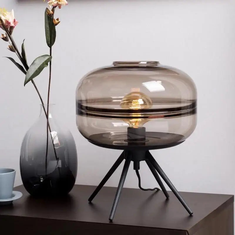 A modern smoked glass desk lamp with tripod base and exposed filament bulb for decorbites glass desk decor