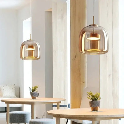 Two modern amber glass led pendant chandeliers with brass accents hang above wooden dining tables