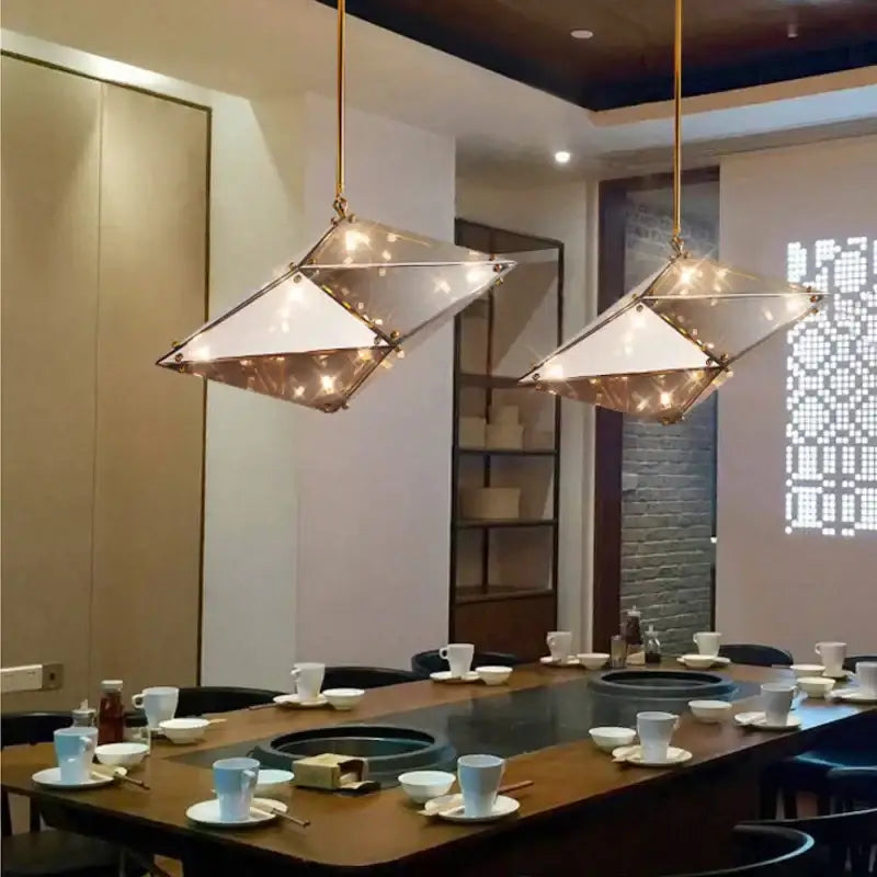 Two smoky gray and amber diamond glass led pendant lights with brass frames hang in a modern living room setting