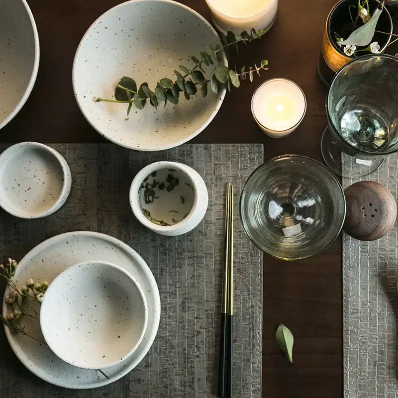 Modern speckled white ceramic dinner plate set featuring a white speckled ceramic bowl with eucalyptus branch inside