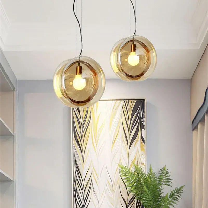 Two amber glass pendant lights with brass accents hang from black cords for modern living space lighting