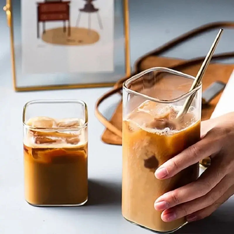 A clear square glass coffee tea mug filled with iced coffee and a gold metal straw for modern kitchen drinkware