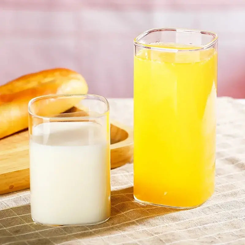 Tall clear glass coffee tea mug with square rim filled with bright yellow juice designed for modern kitchen use