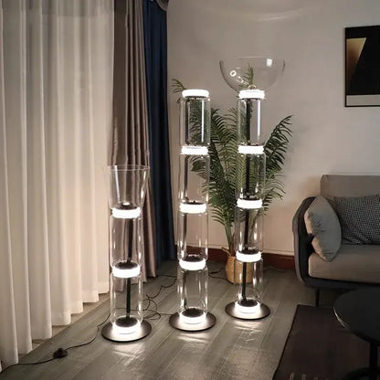 Three modern glass led floor lamps with stacked cylindrical transparent bodies and illuminated white led rings for living room lighting