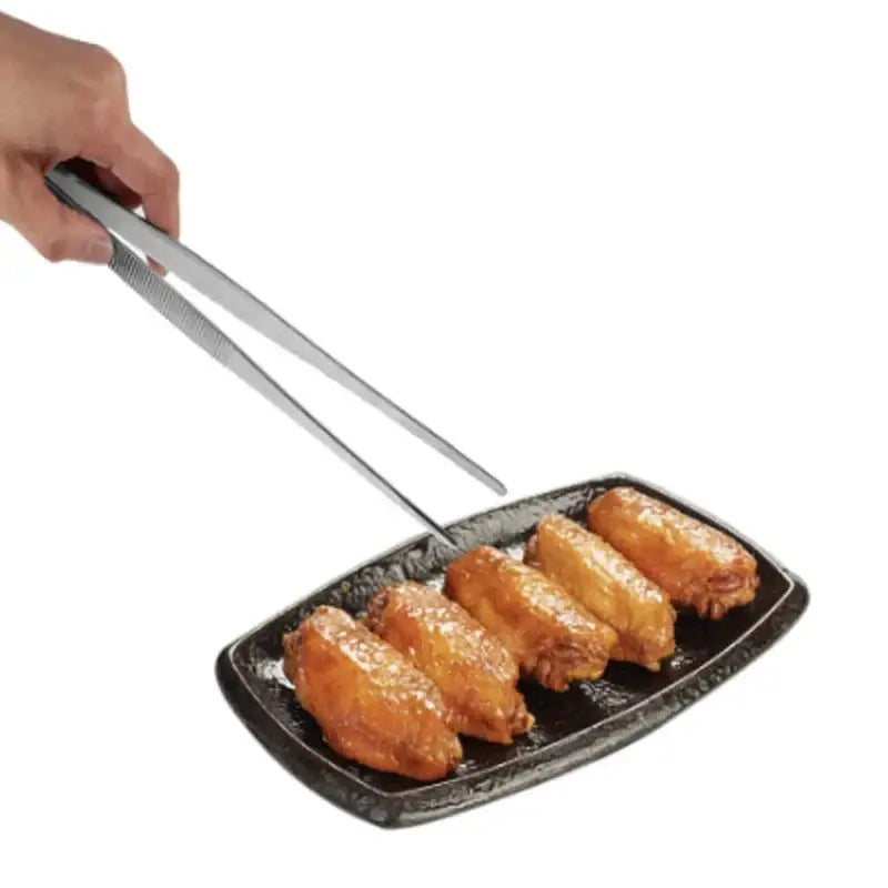 Silver stainless steel bbq tongs with textured grip picking up fried chicken wings on black cast iron plate enhancing grilling experience