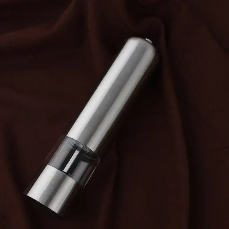 A sleek stainless steel electric salt pepper grinder with a transparent glass section showing peppercorns inside