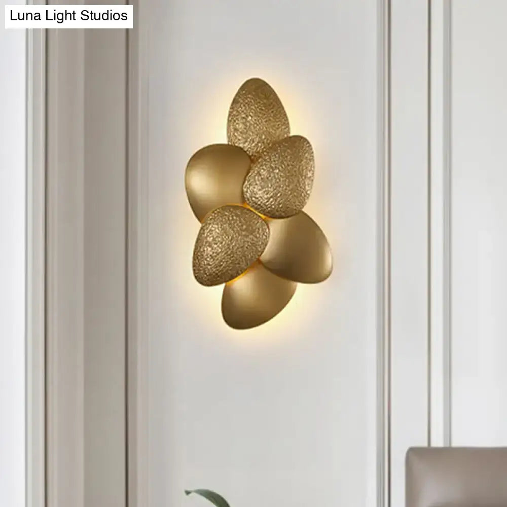 Gold-toned stainless steel squama wall light with five petal-like elements emitting a warm glow for bedroom use