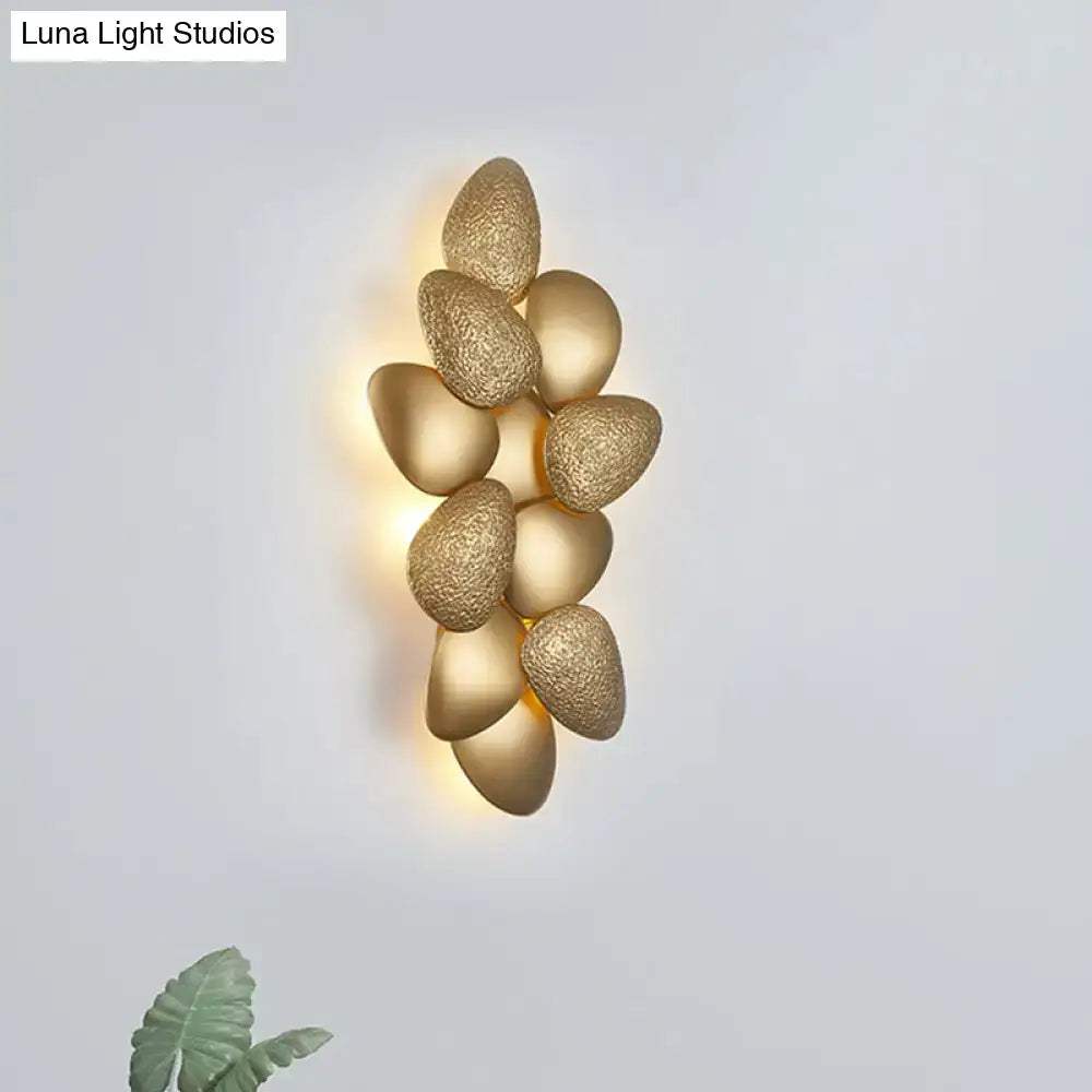 Gold-toned modern stainless steel squama wall light featuring textured egg-shaped elements in a cascading design for bedroom use