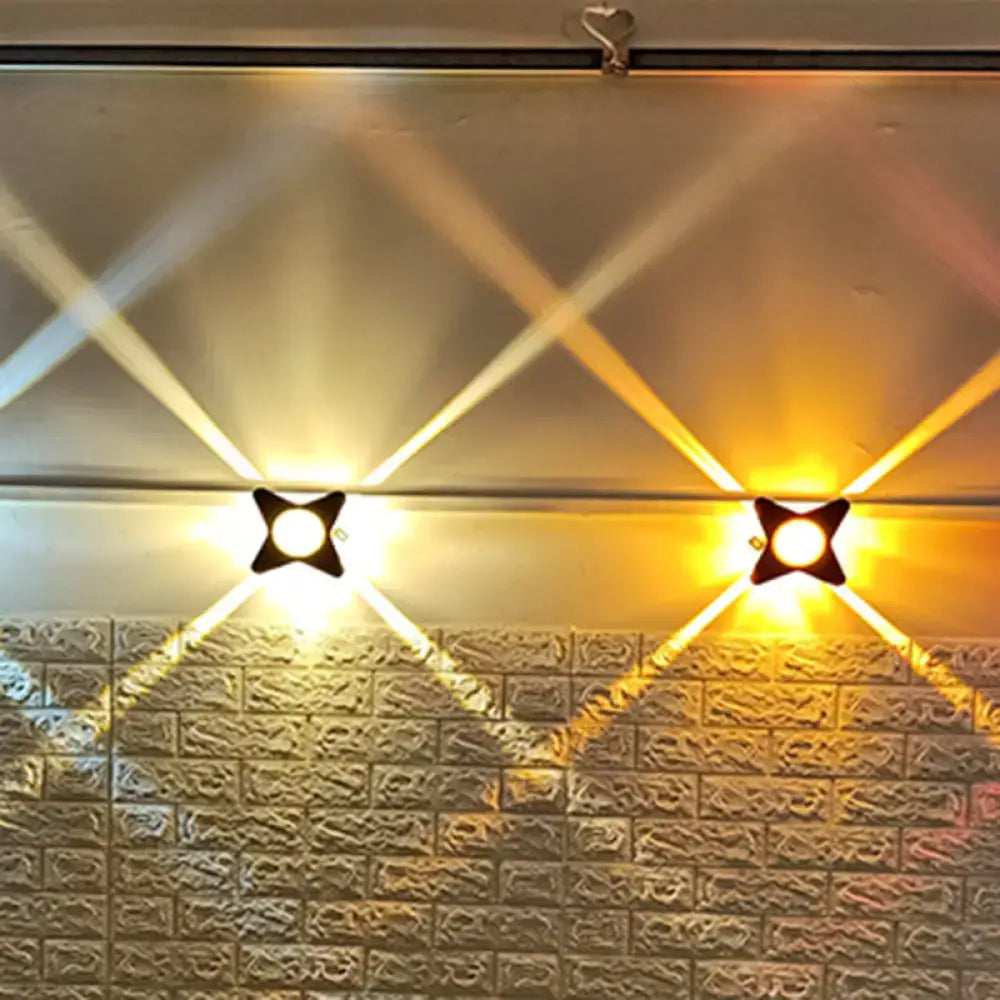 Two black star-shaped modern star petals outdoor wall sconces emit warm yellow led light on textured brick wall