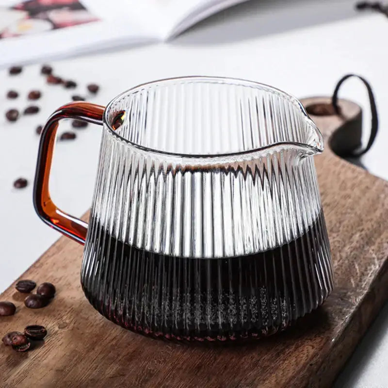 Modern striped glass coffee pot with vertical ridges and amber handle filled with dark brewed coffee