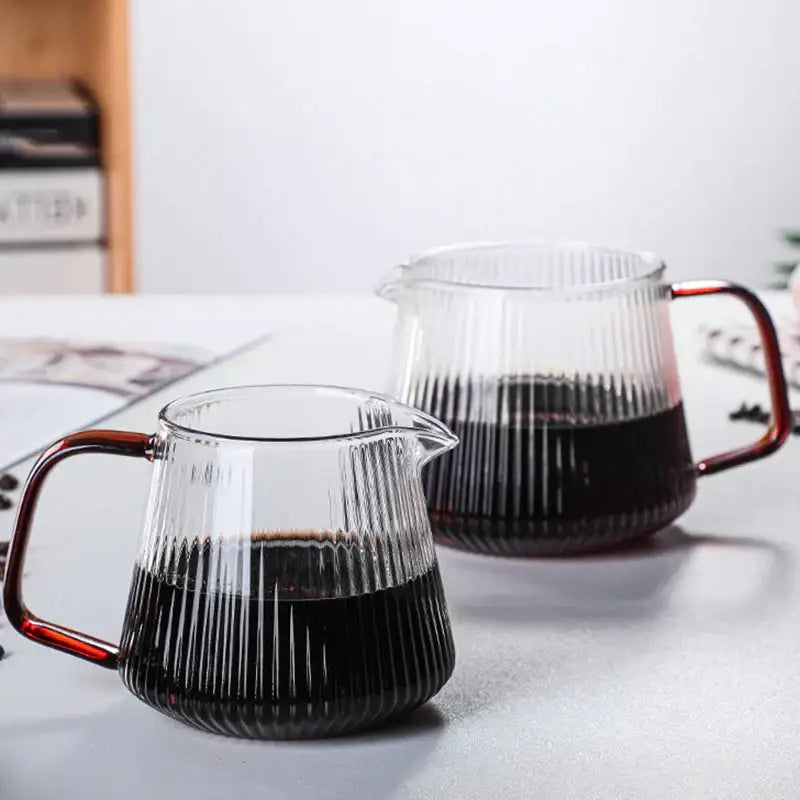 Modern striped glass coffee pot with vertical ribbed texture and amber copper handle filled with dark coffee liquid