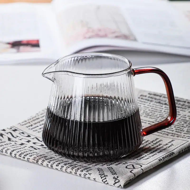 Modern striped glass coffee pot with vertical ribbed texture and amber handle filled with dark liquid for brewing coffee