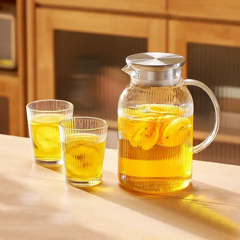 Modern striped glass cold water kettle set with clear glass pitcher filled with lemon slices and silver lid and handle