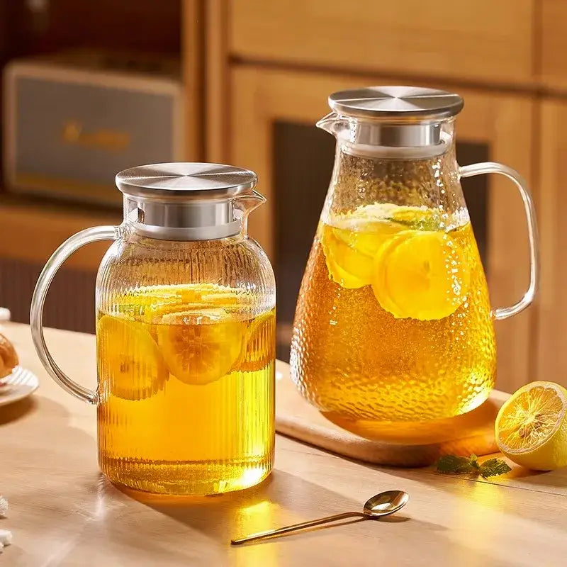 Modern striped glass cold water kettle set with textured clear glass pitchers and silver lids filled with lemon liquid